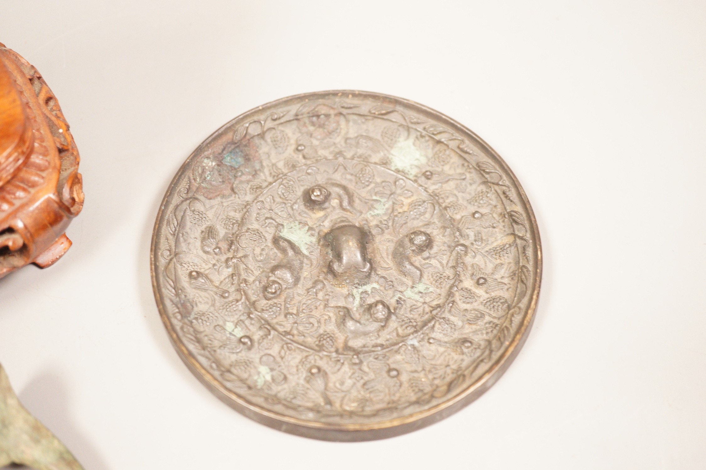 A Chinese bronze mirror, 11cm diameter, a jadeite floral carving on stand with a metal relief plaque, and a pair of bracelets